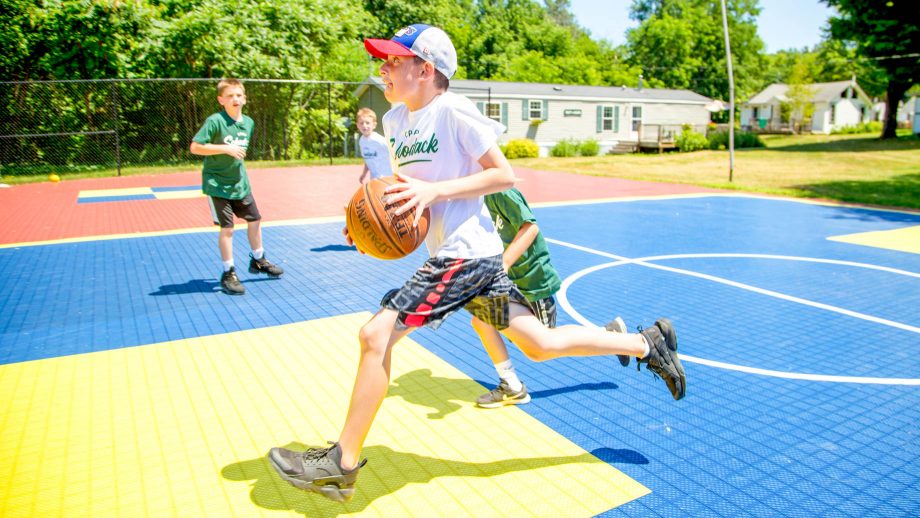 Boy runs with basketball during summer camp game