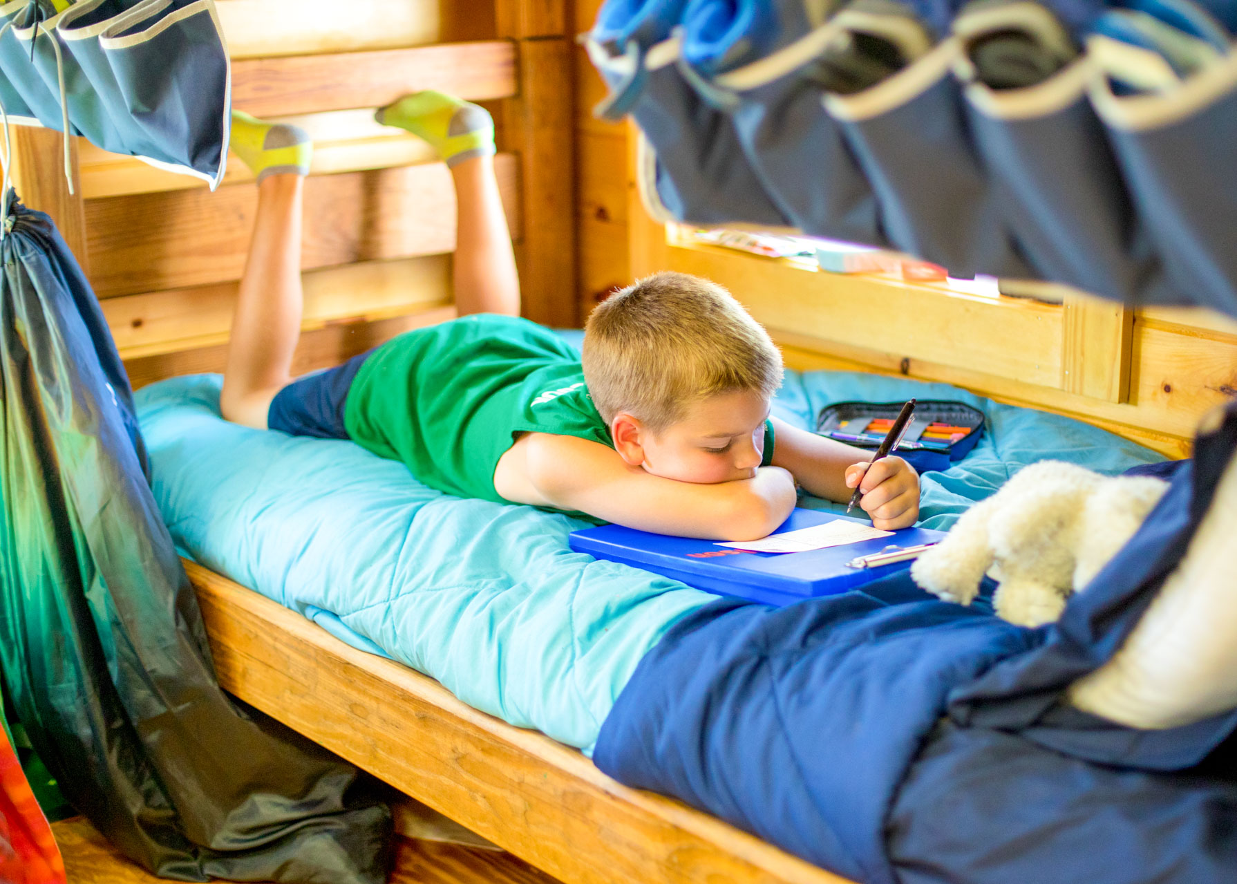 Young boy lies on camp bunk to write