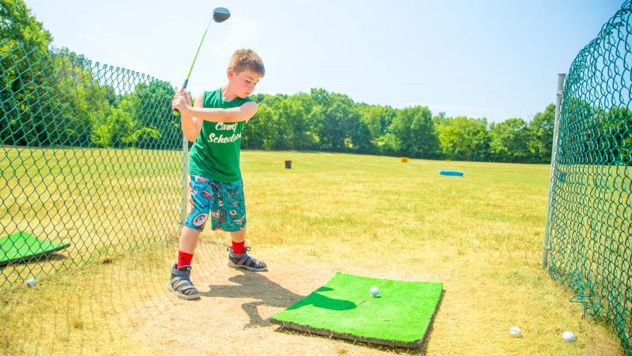 Boy swing golf club at summer camp driving range