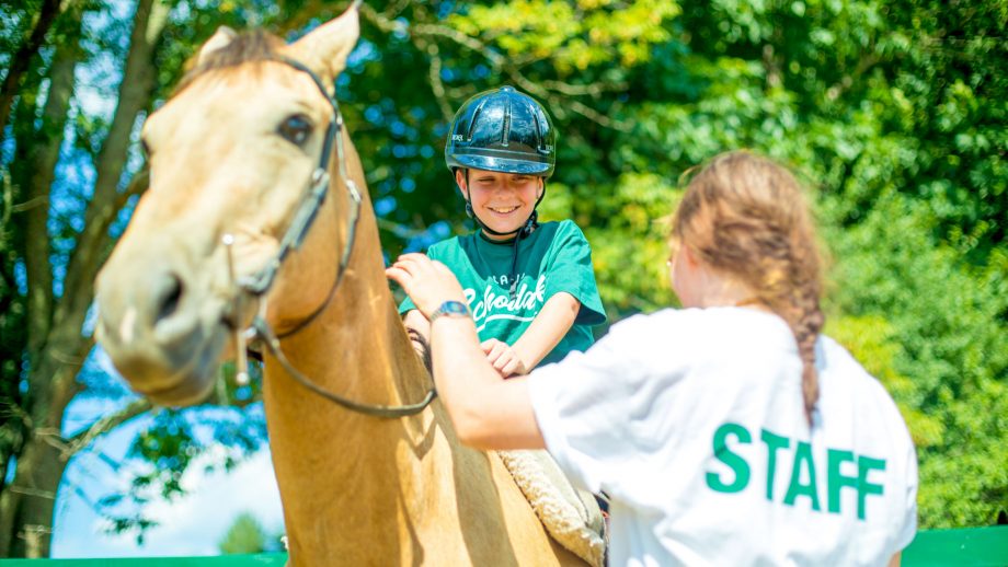 Boy smiles at camp staff member from back of horse