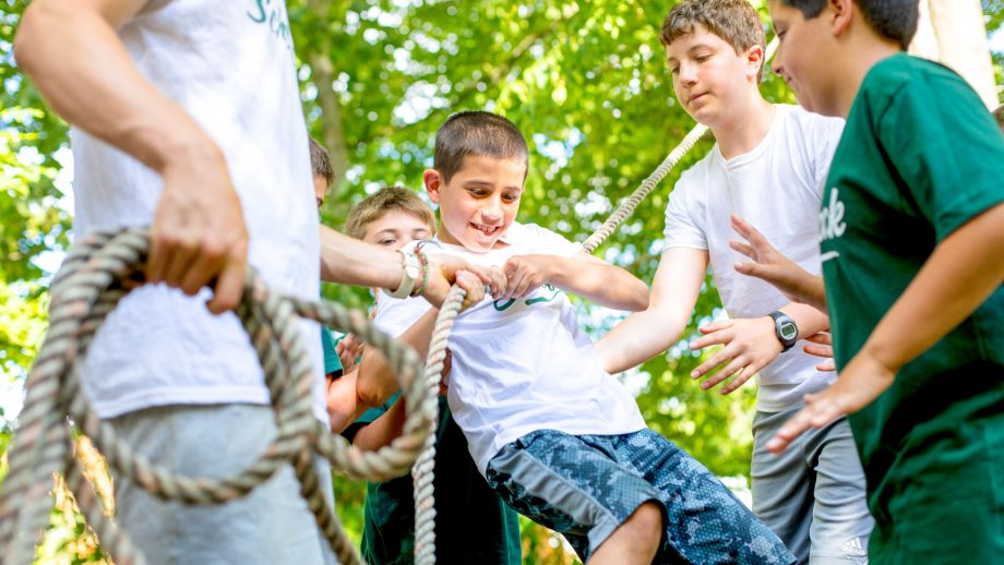 Group of campers support boy on low ropes course