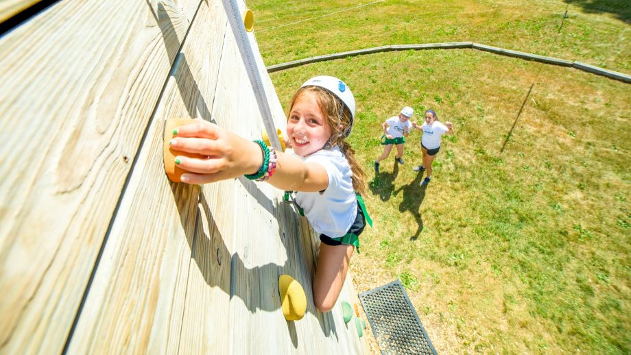 Girl reaches for handhold on rock climbing wall