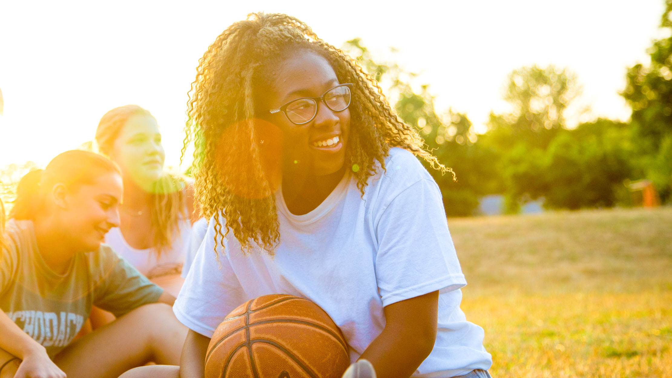 Smiling girl holds basketball at sunset