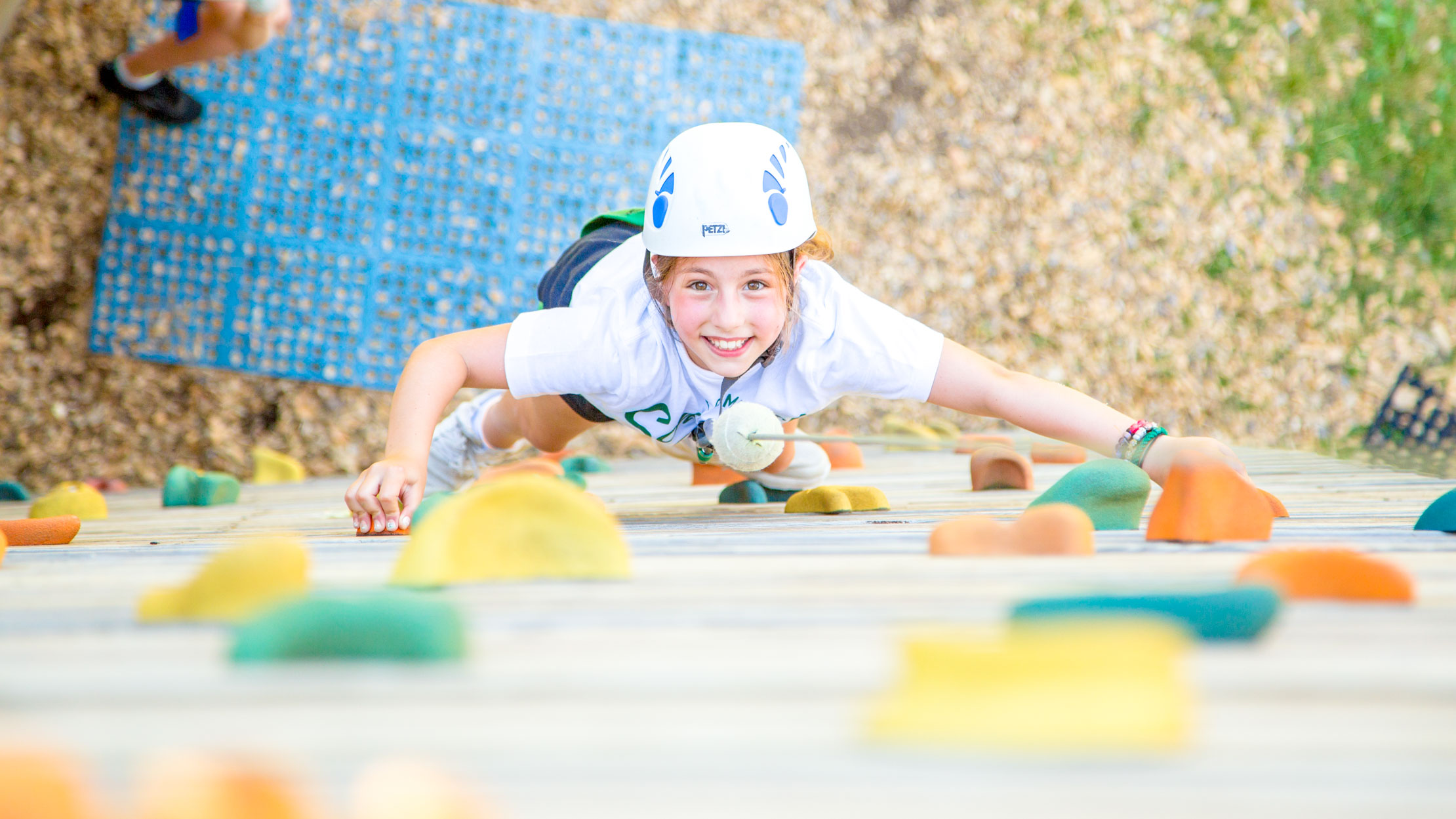 Smiling girl climbs rock wall at summer camp