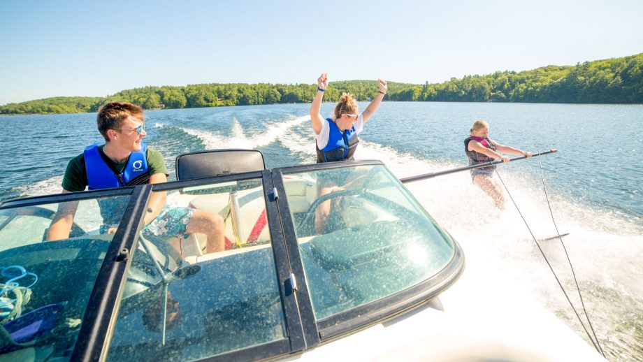 Staff member on speedboat cheers for waterskiing camper