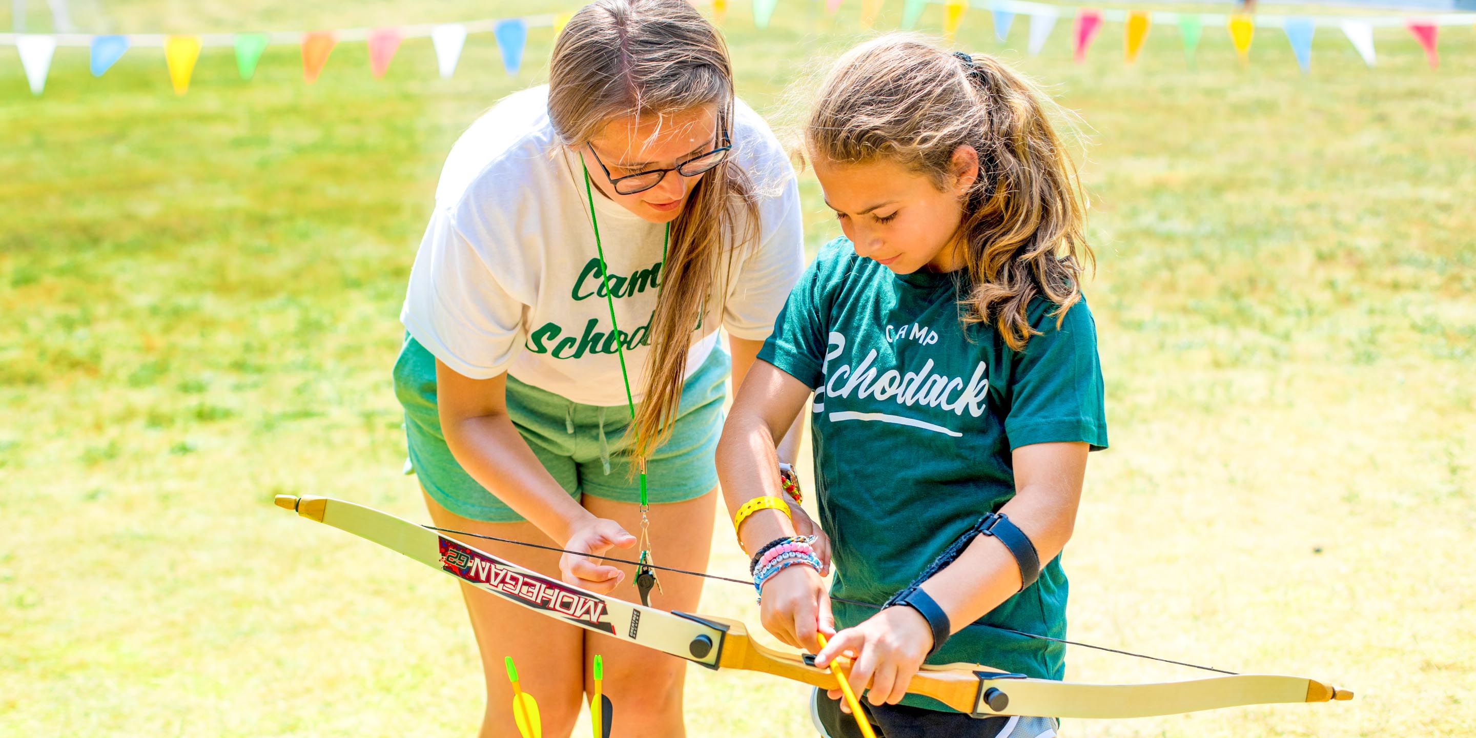 Staff member helps camper nock arrow for archery