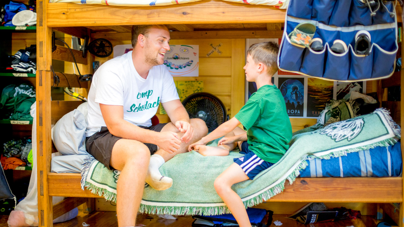 Counselor and camper sit on bunk to chat