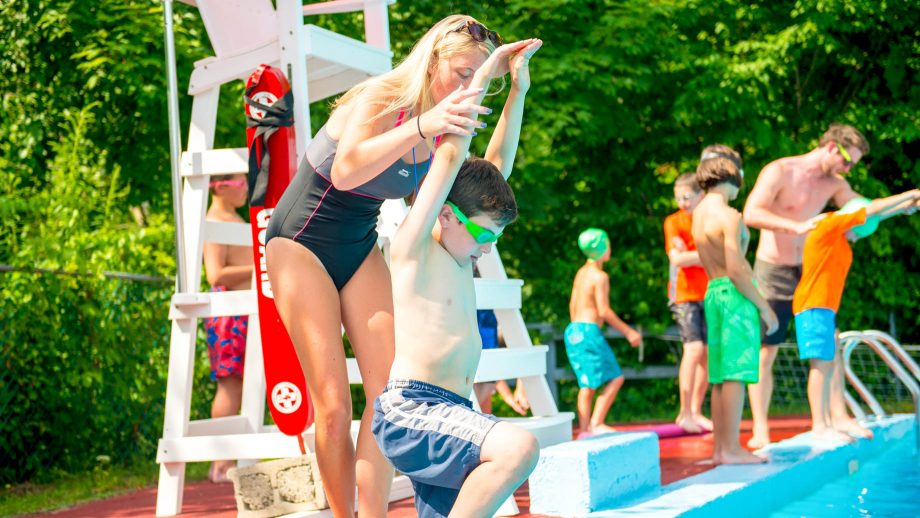 Lifeguard helps camper practice dive form