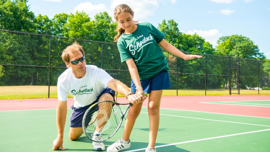 Staff member helps camper with tennis swing