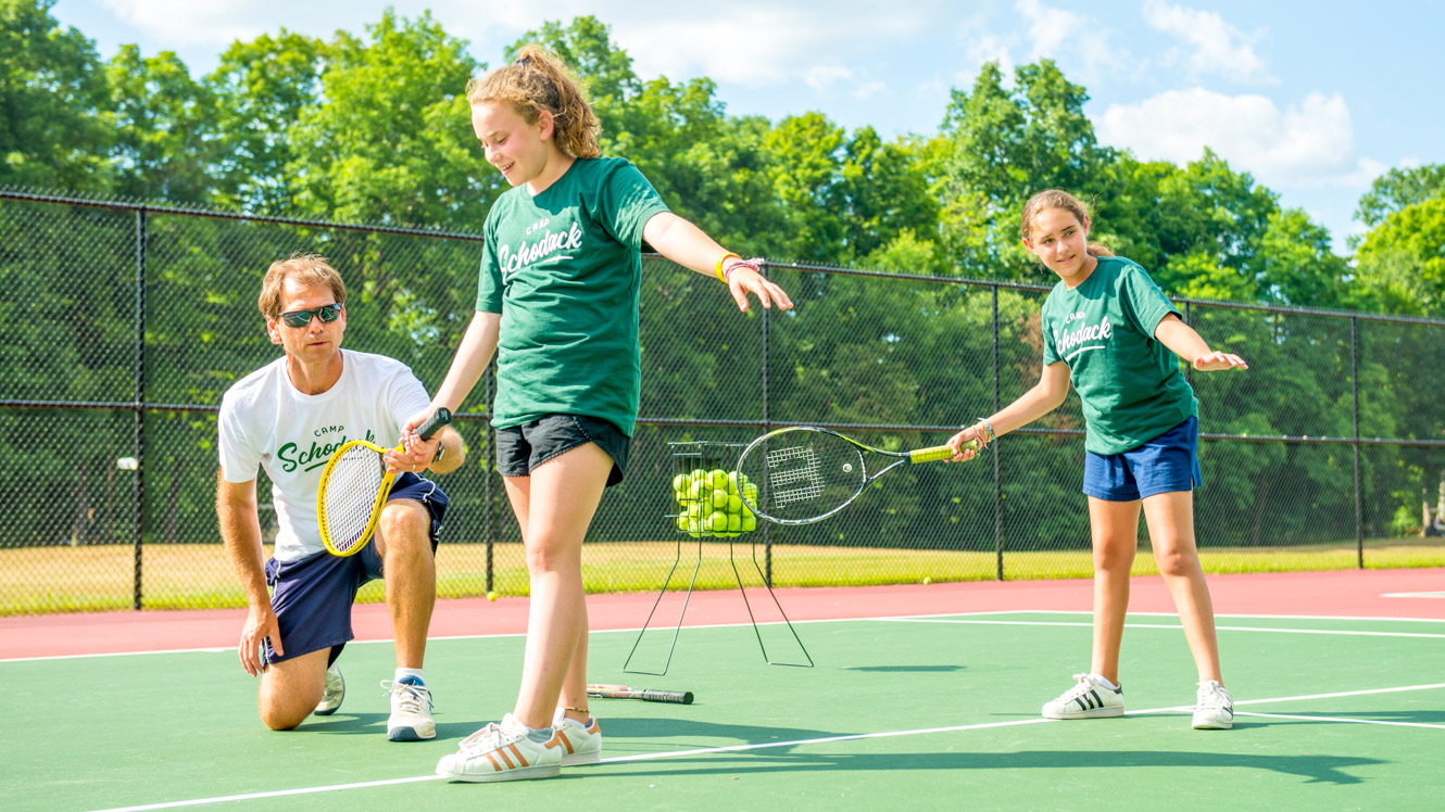 Staff member helps campers with tennis swing