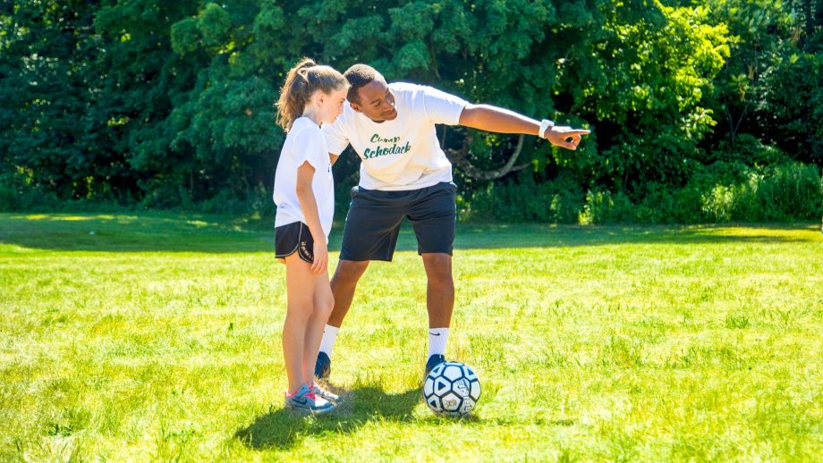 Staff member helps girl practice soccer at summer camp