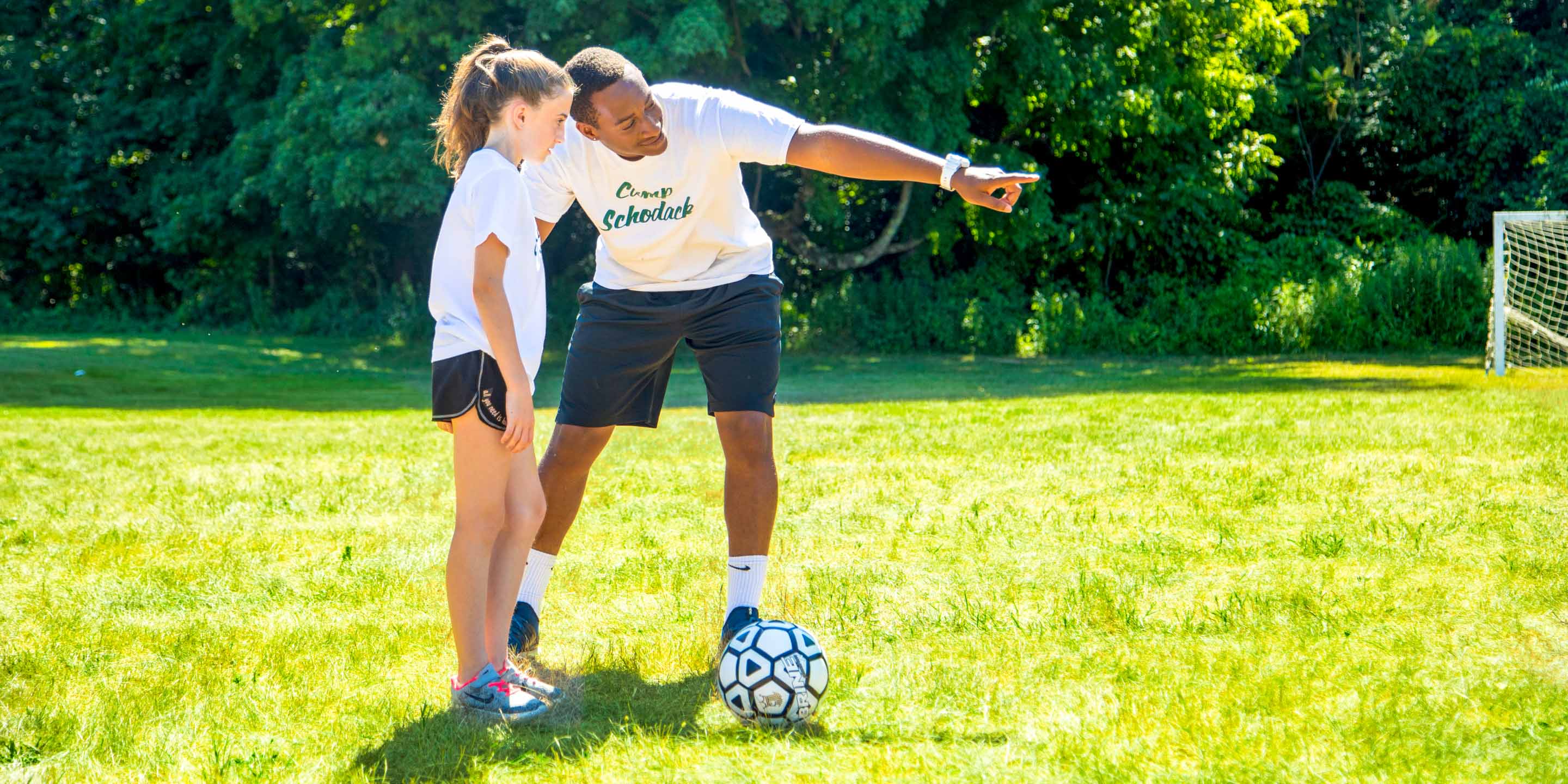 Staff member helps girl practice soccer at summer camp