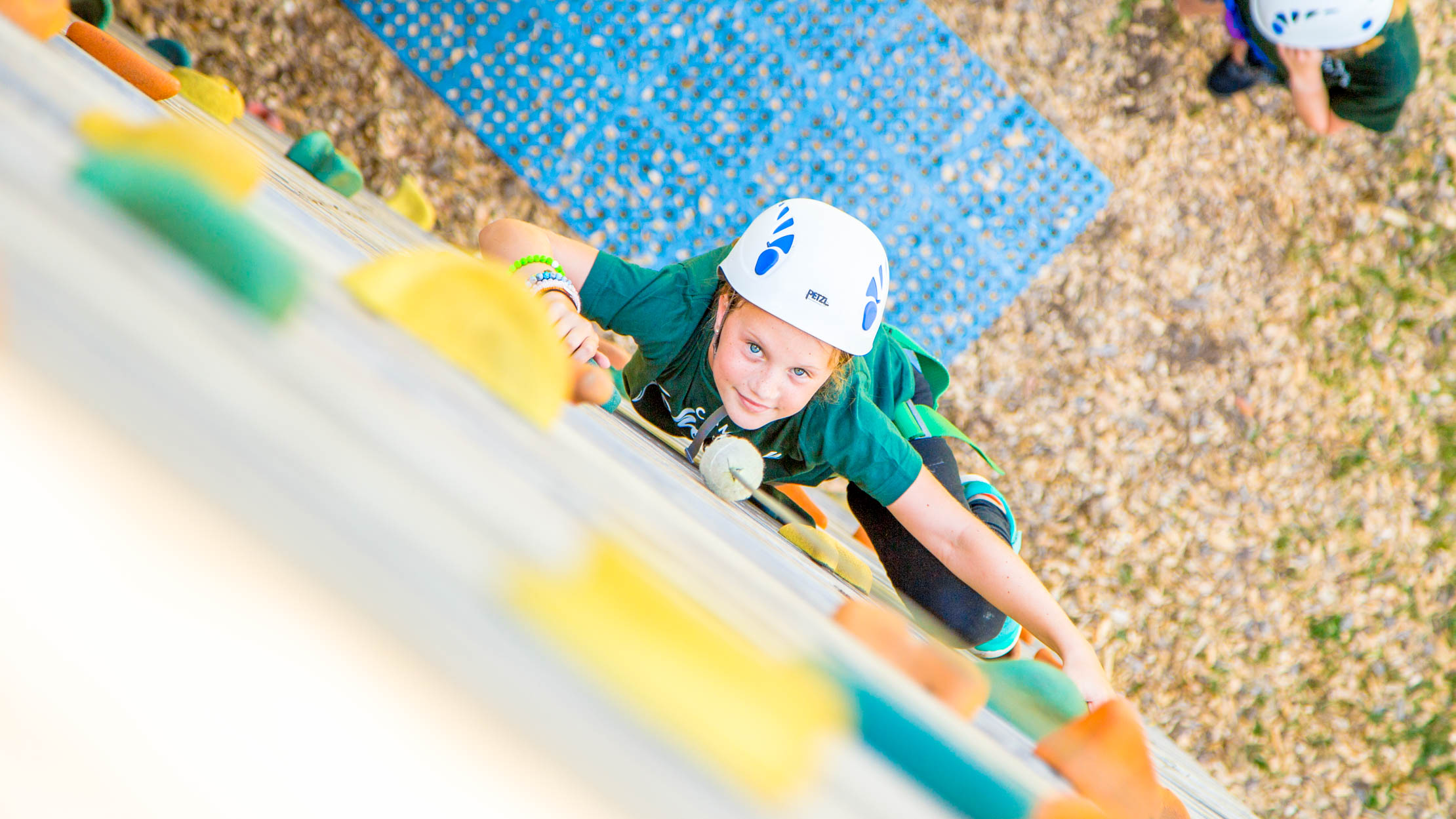 Girl climbs wall toward camera at summer camp