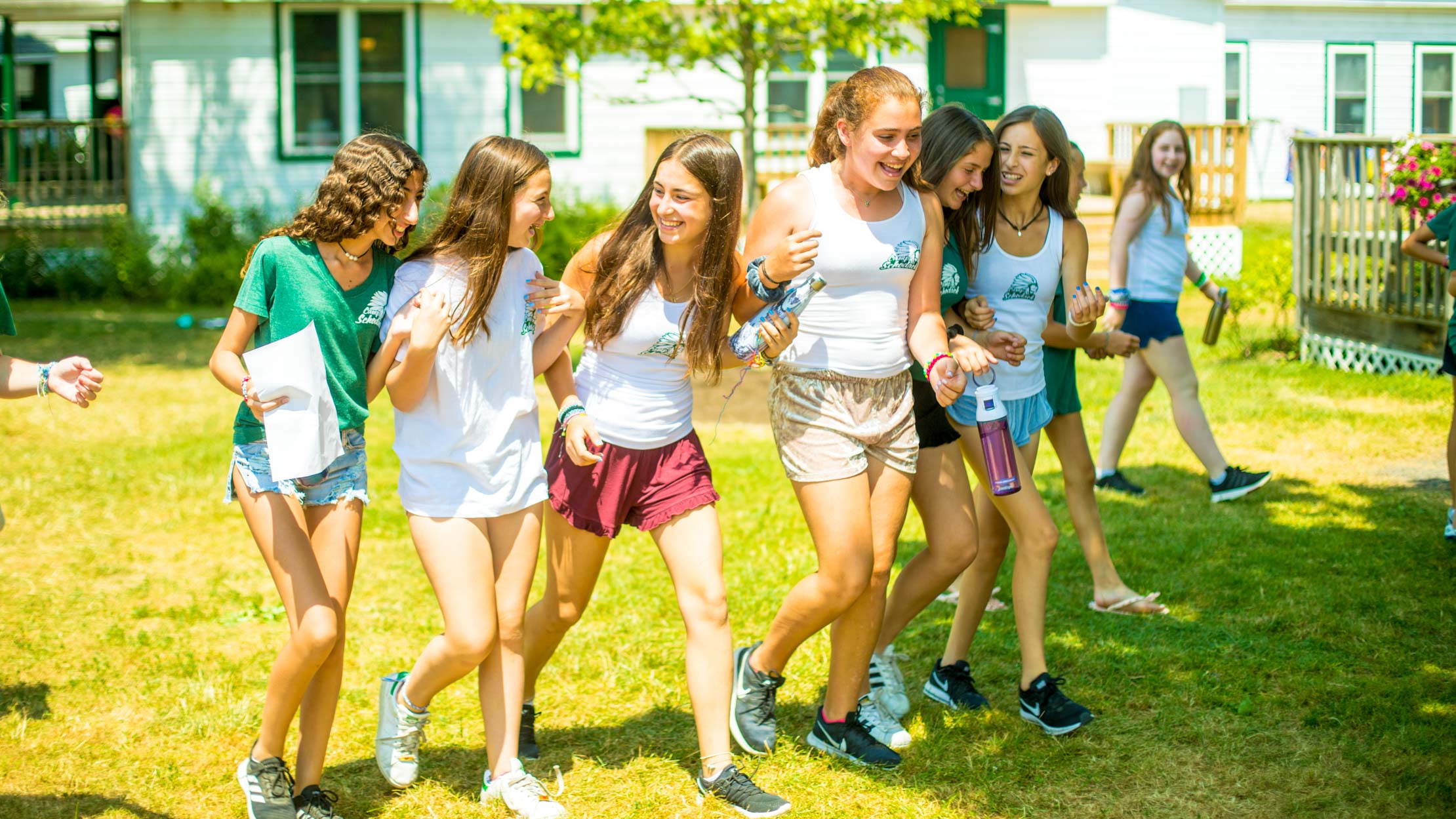 Girls laugh while walking across summer camp lawn