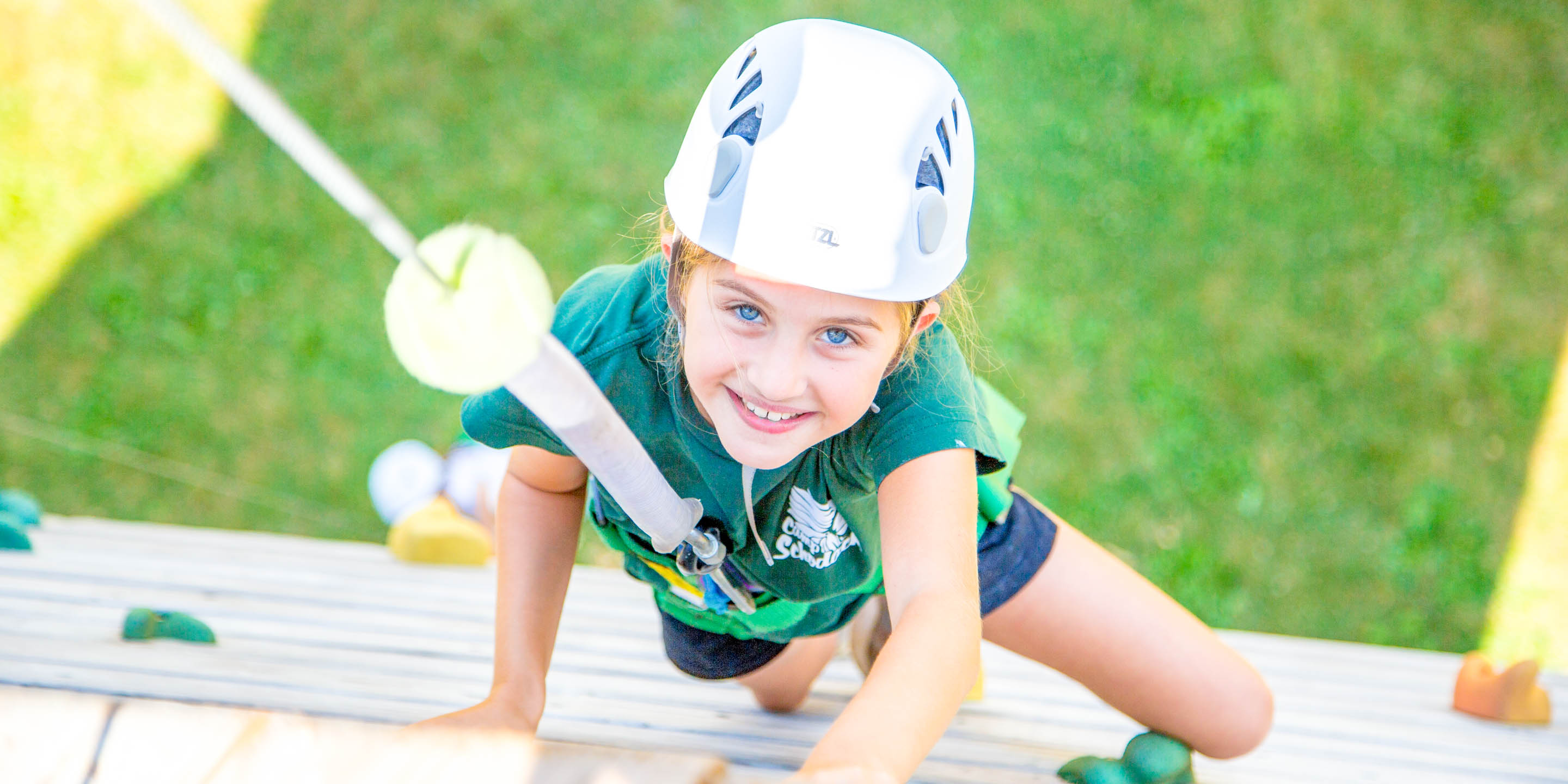 Smiling girl climbs rock wall toward camera