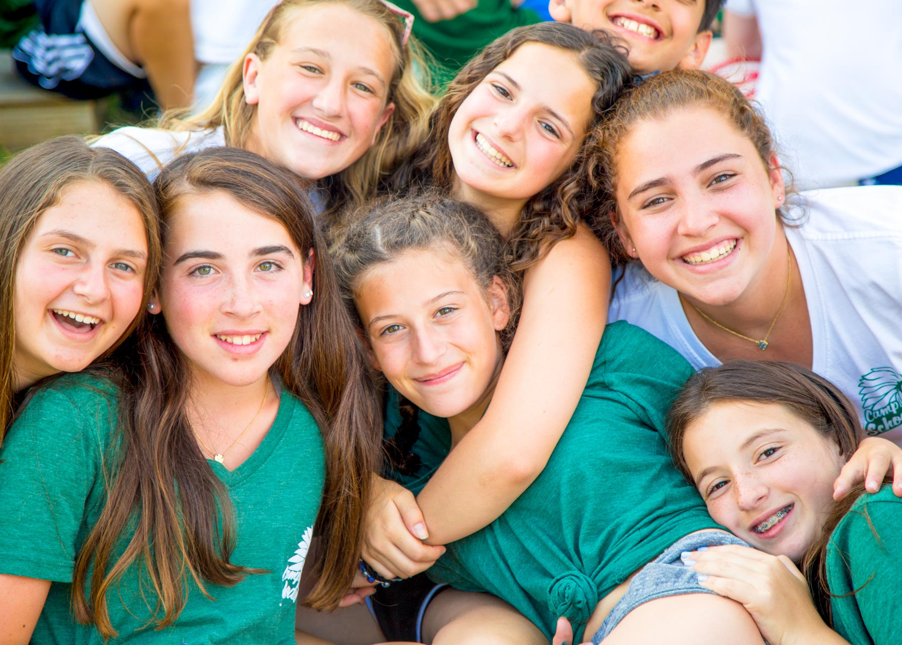 A group of smiling girls hug each other at summer camp