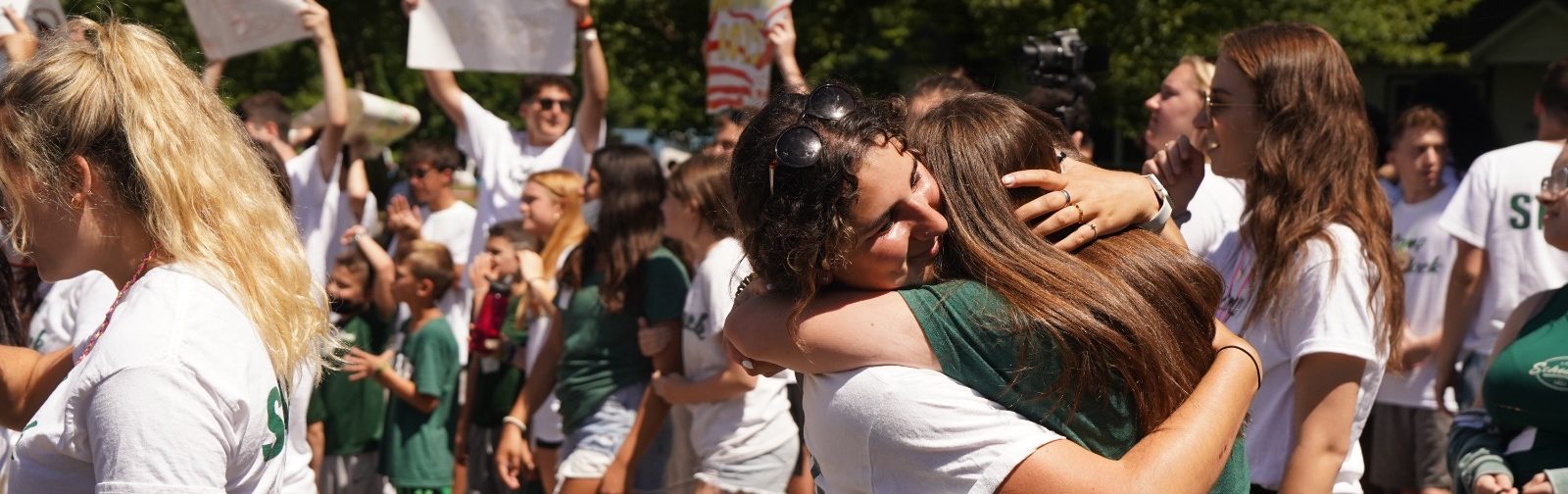 A staff member and camper greet eachother with a big hug