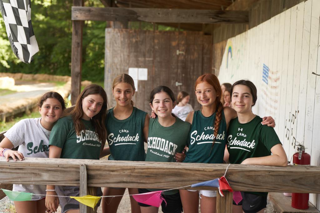 Girls standing behind a wooden banister, they are smiling and standing close together.